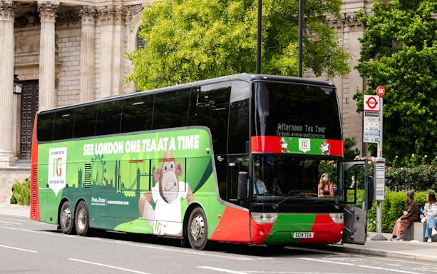 Double-decker bus for Afternoon Tea Sightseeing Tour in London, parked near historic building.
