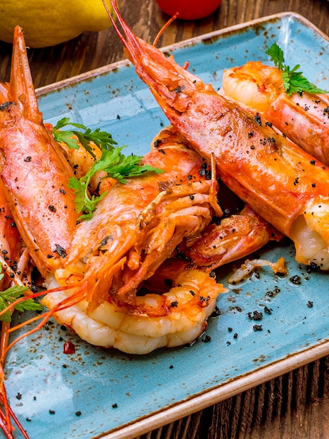 Tiger prawns garnished with herbs and lemon slices on a blue plate.