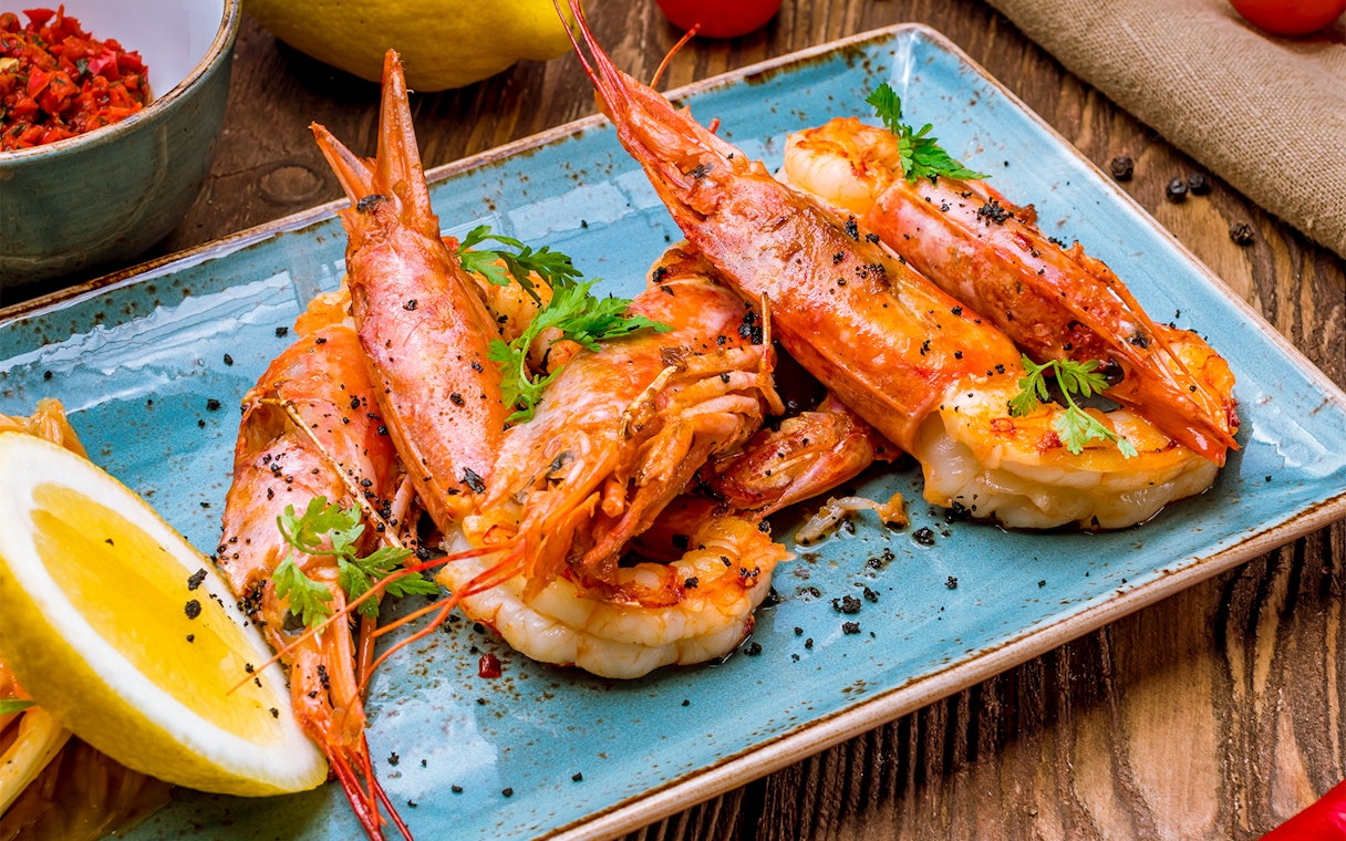 Tiger prawns garnished with herbs and lemon slices on a blue plate.