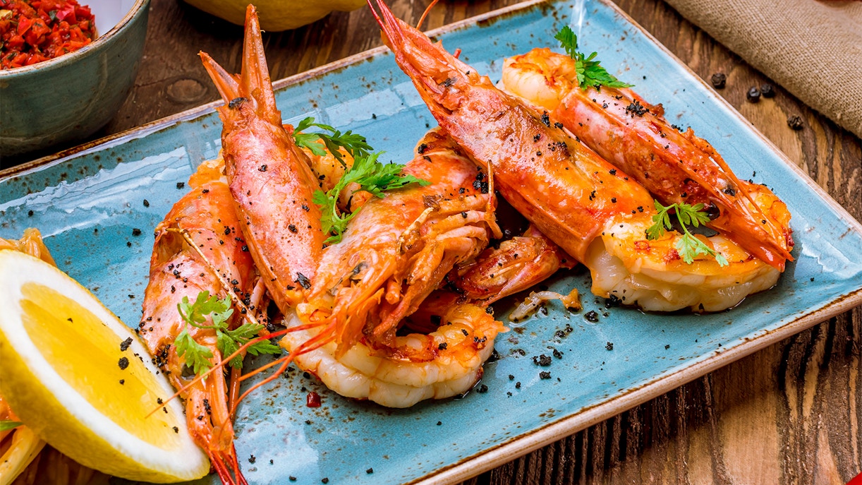 Tiger prawns garnished with herbs and lemon slices on a blue plate.