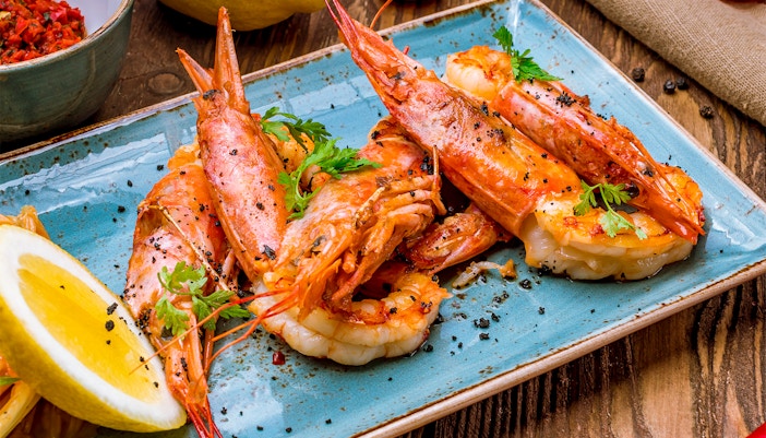 Tiger prawns garnished with herbs and lemon slices on a blue plate.