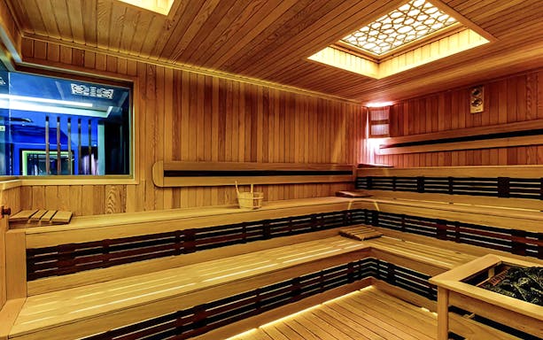 Interior of a wooden Turkish bath with benches and a central heating area.