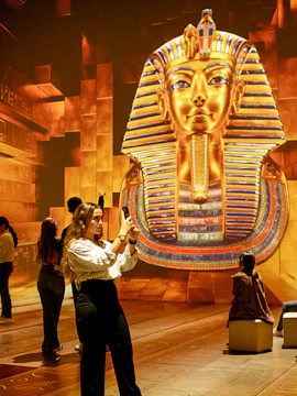 Visitors photographing a large digital display of Tutankhamun's mask at an exhibition.