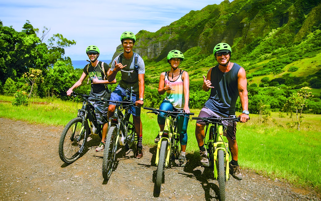 Group of cyclists on e-bikes at Kualoa Ranch, lush mountains in background.