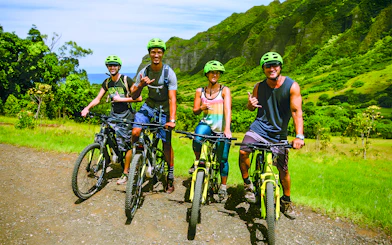 Group of cyclists on e-bikes at Kualoa Ranch, lush mountains in background.