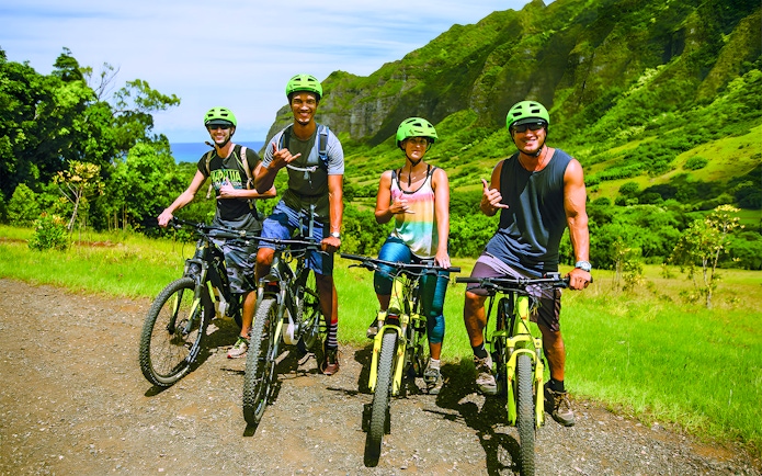 Group of cyclists on e-bikes at Kualoa Ranch, lush mountains in background.