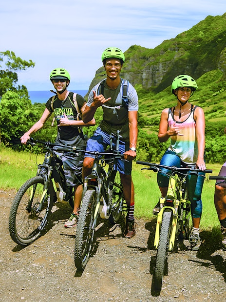 Group of cyclists on e-bikes at Kualoa Ranch, lush mountains in background.