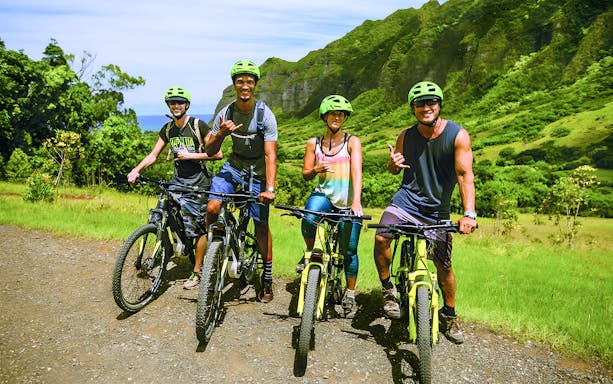 Group of cyclists on e-bikes at Kualoa Ranch, lush mountains in background.