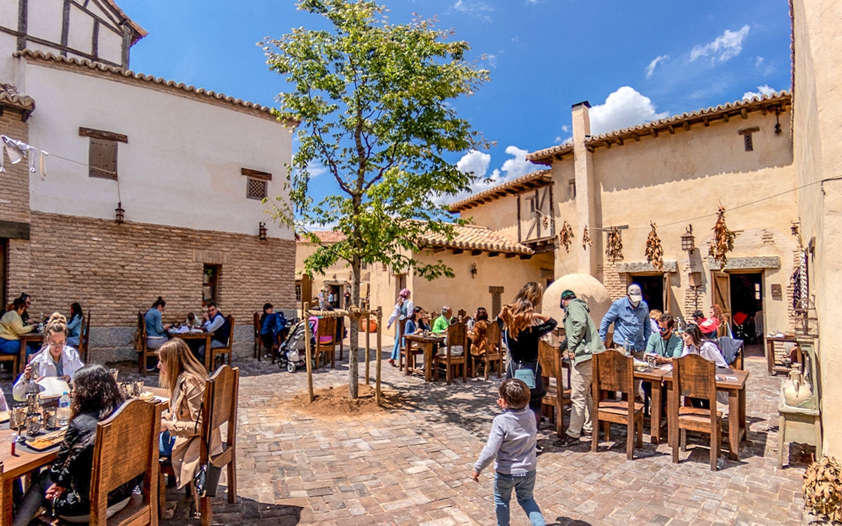 Visitors dining outdoors at a rustic village setting in Puy du Fou Park.