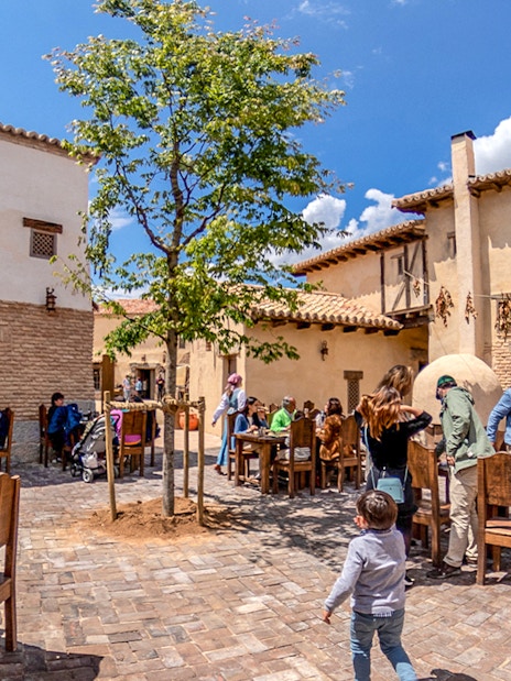 Visitors dining outdoors at a rustic village setting in Puy du Fou Park.