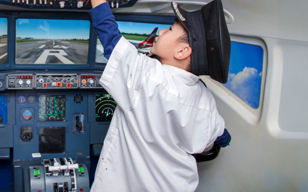 Child in pilot uniform exploring airplane cockpit at KidZania Singapore.