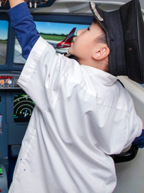 Child in pilot uniform exploring airplane cockpit at KidZania Singapore.