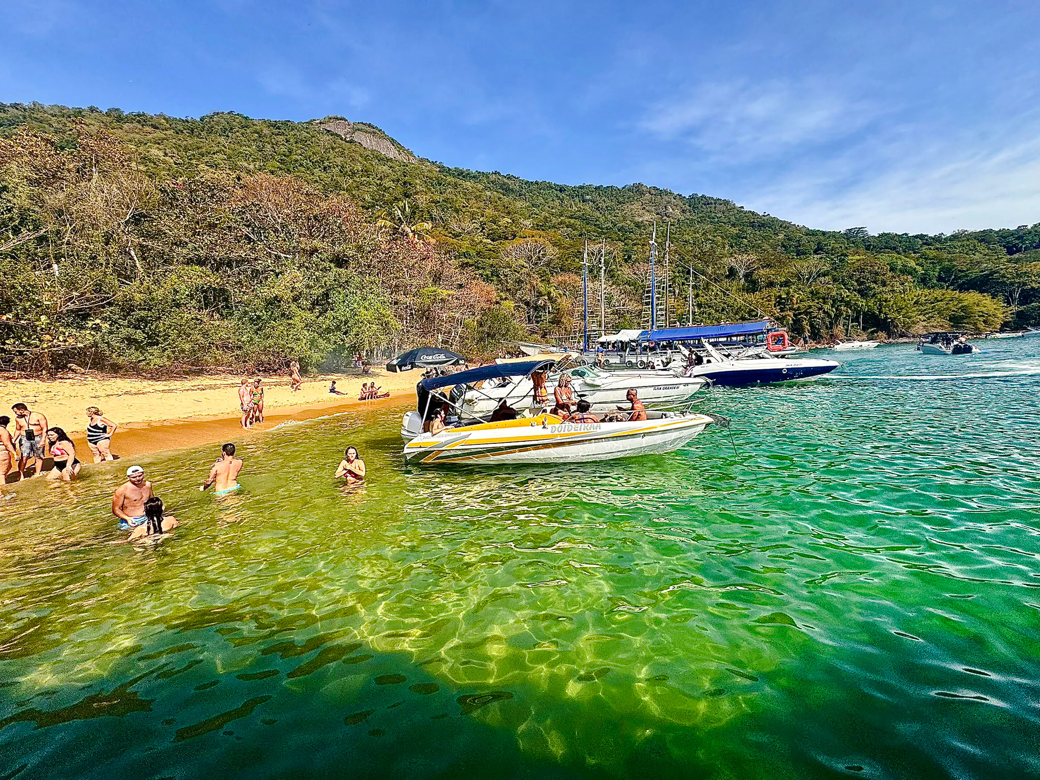Boats anchored near a beach with people swimming in Arraial do Cabo, Brazil.