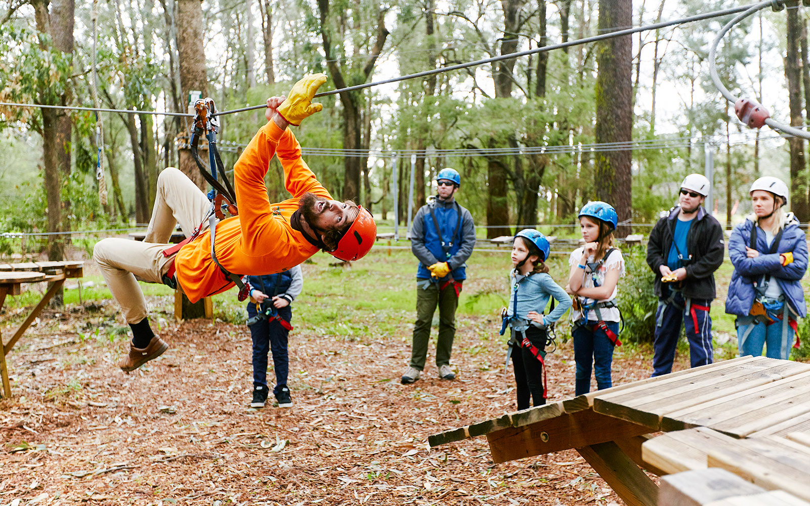 Person zip-lining in Ludlow Tuart Forest, Western Australia, with onlookers in safety gear.