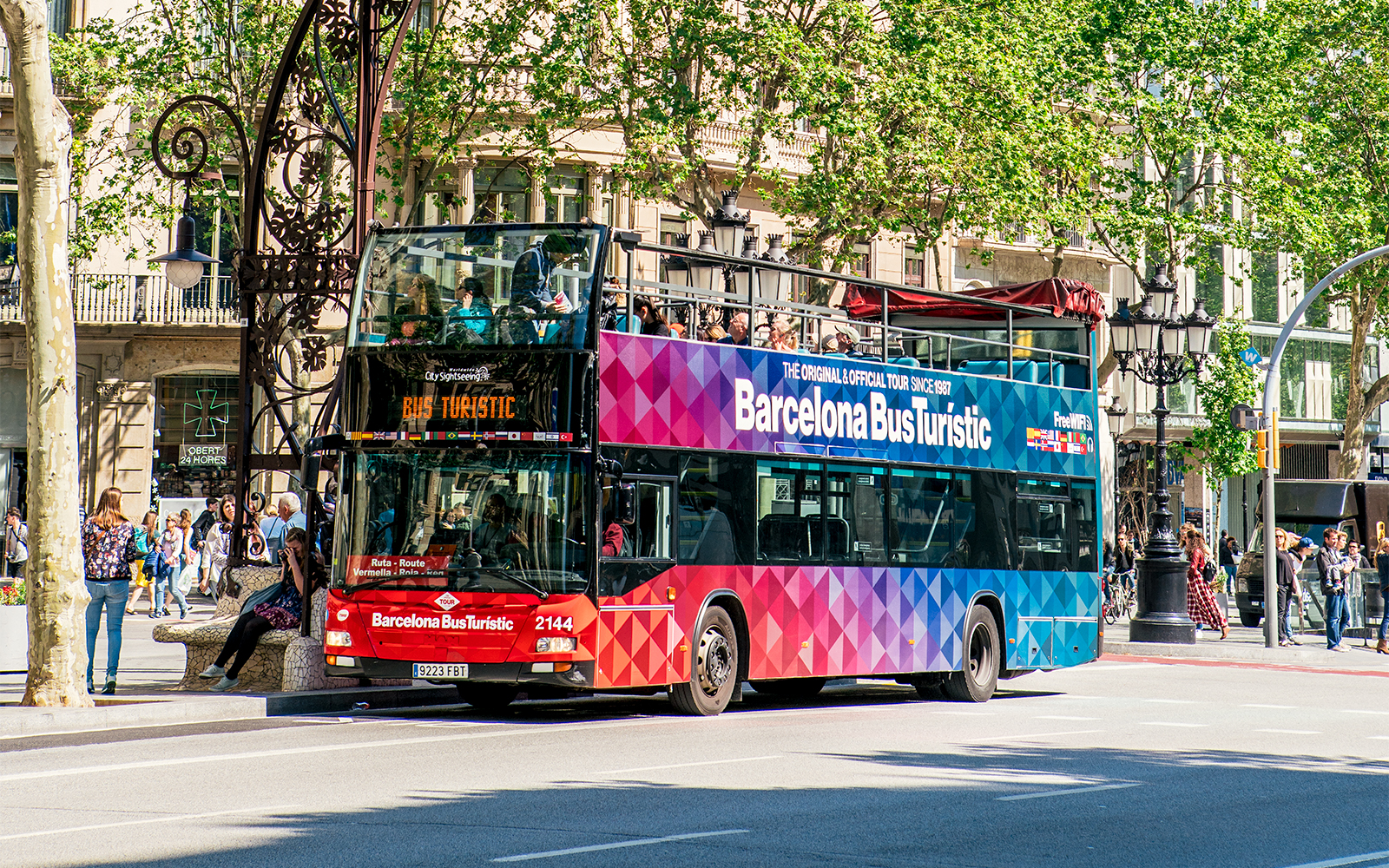 Barcelona Bus Turistic double-decker on city street with passengers on top deck.