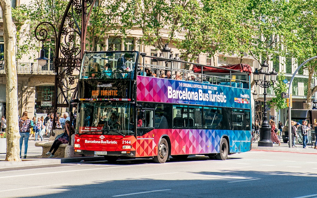 Barcelona Bus Turistic double-decker on city street with passengers on top deck.