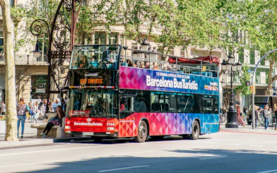 Barcelona Bus Turistic double-decker on city street with passengers on top deck.