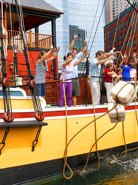 Tourists reenacting the Boston Tea Party by throwing tea chests from a ship in Boston Harbor.
