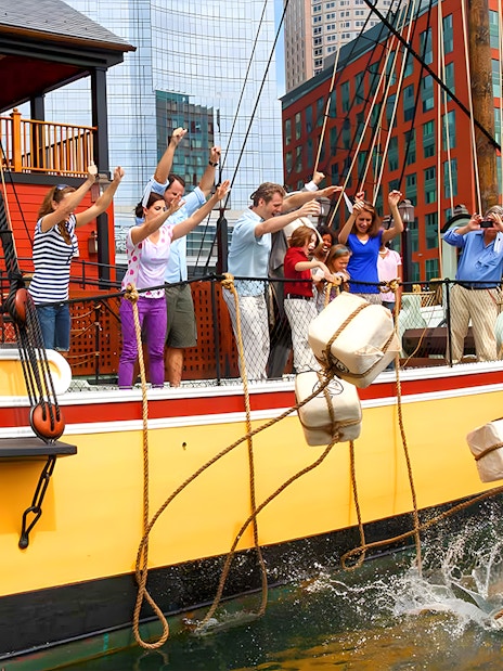 Tourists reenacting the Boston Tea Party by throwing tea chests from a ship in Boston Harbor.