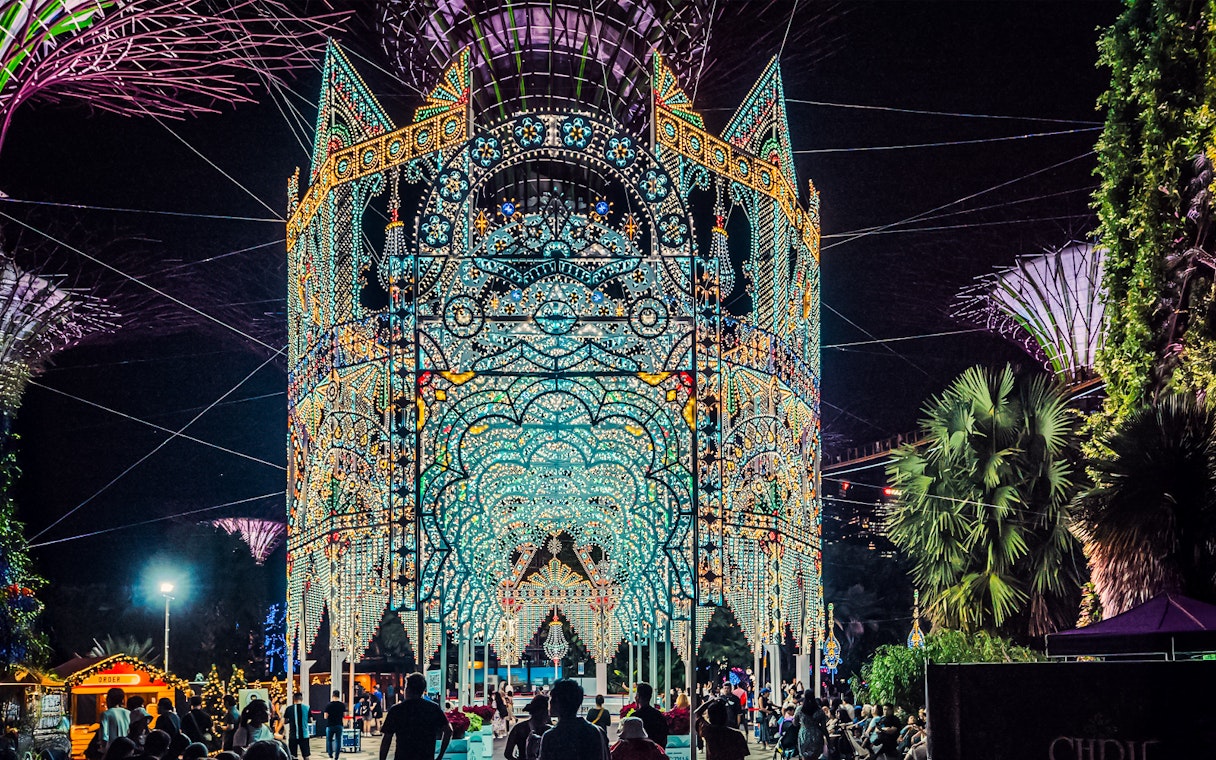 Christmas light display at Gardens by the Bay, Singapore, with people admiring the illuminated structure.