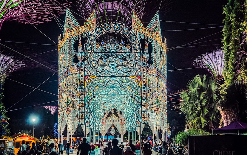 Christmas light display at Gardens by the Bay, Singapore, with people admiring the illuminated structure.