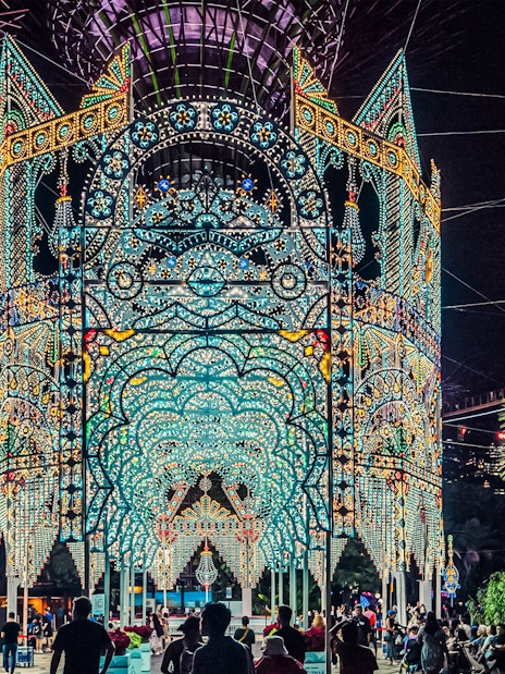 Christmas light display at Gardens by the Bay, Singapore, with people admiring the illuminated structure.