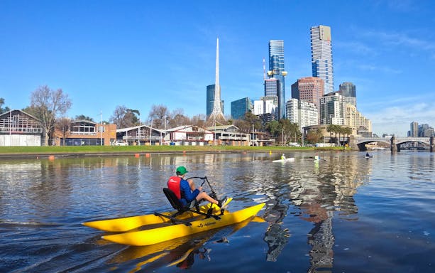 Person on a yellow waterbike on Yarra River with Melbourne skyline in the background.