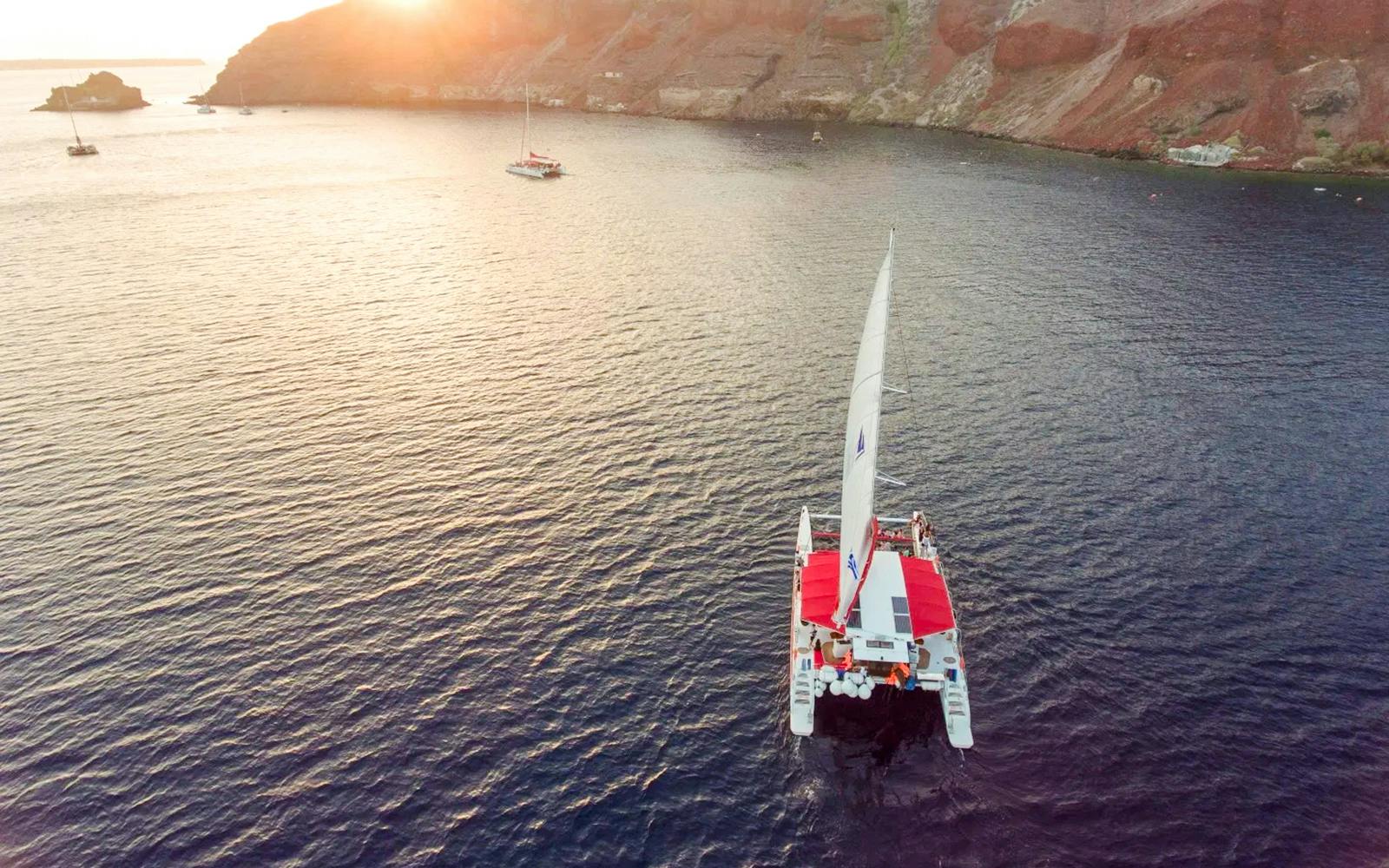 Catamaran sailing at sunset near rocky coastline on the Red Cruise.