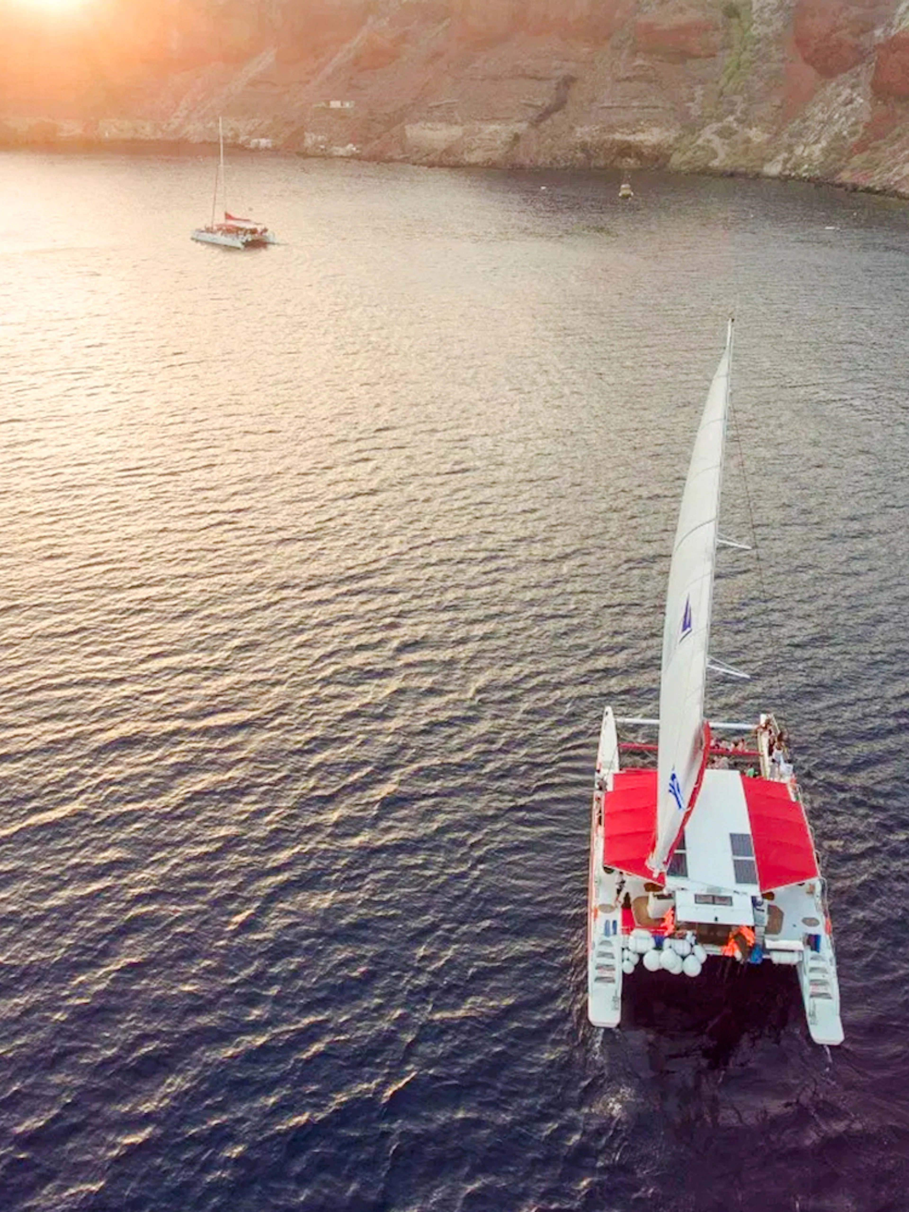 Catamaran sailing at sunset near rocky coastline on the Red Cruise.
