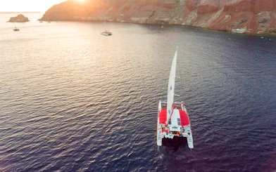 Catamaran sailing at sunset near rocky coastline on the Red Cruise.