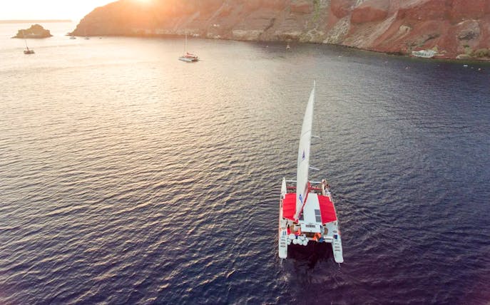 Catamaran sailing at sunset near rocky coastline on the Red Cruise.