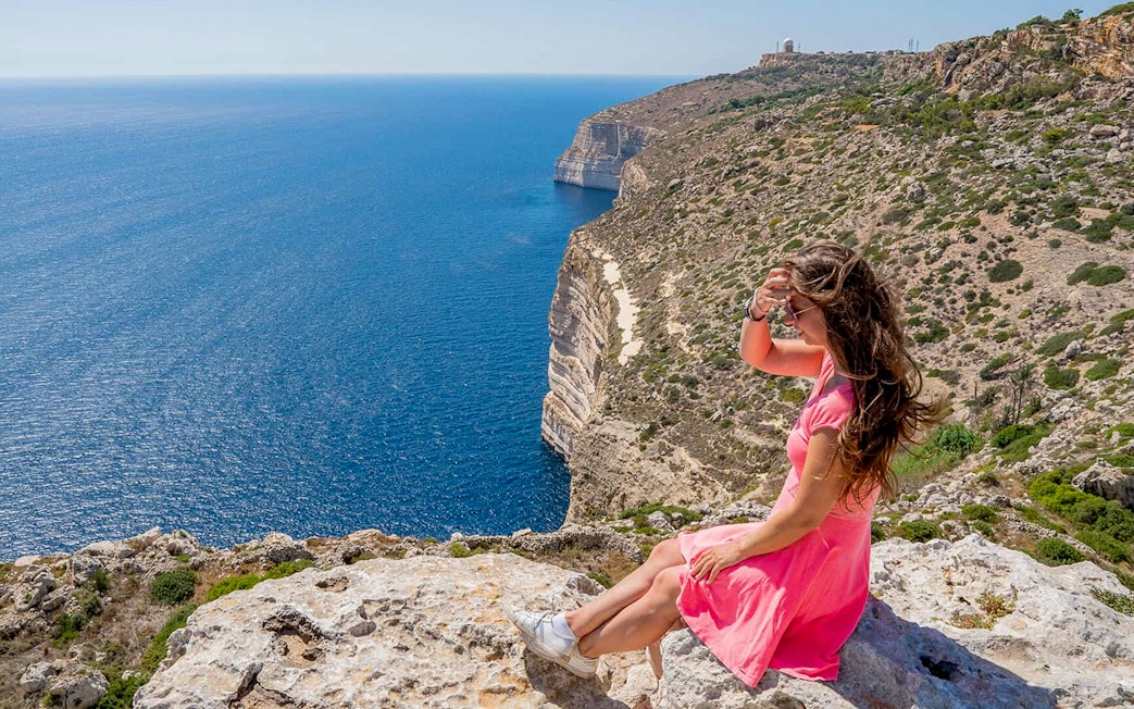 Woman sitting on Dingli Cliffs overlooking the sea, Malta.