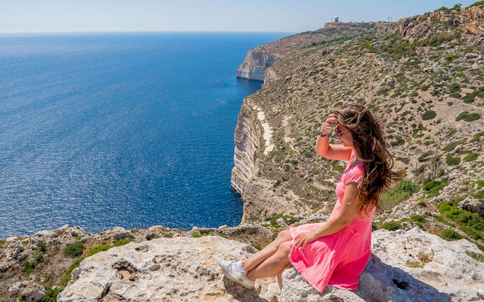 Woman sitting on Dingli Cliffs overlooking the sea, Malta.