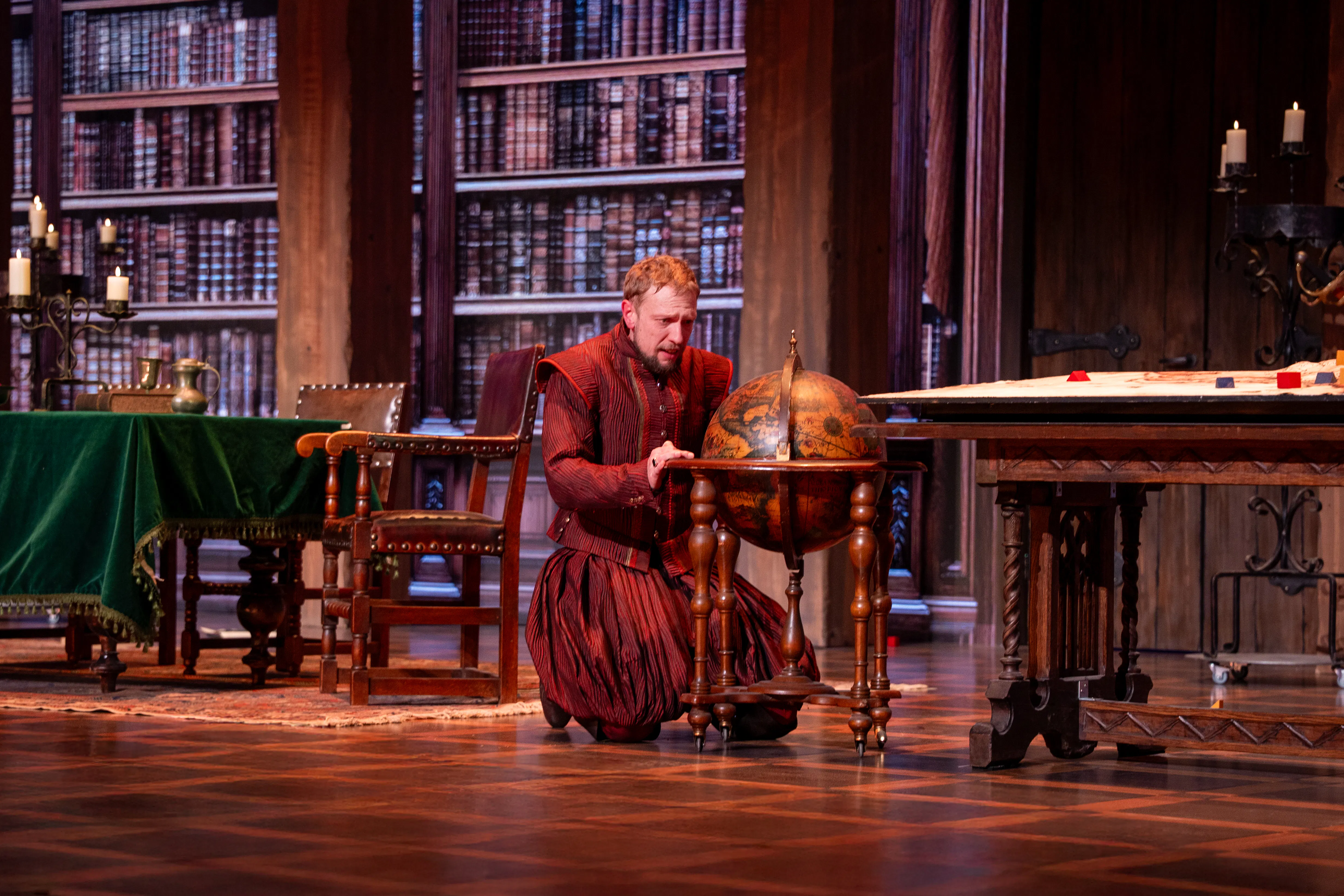 Man in historical attire examining a globe in a library setting, related to Willem van Oranje.