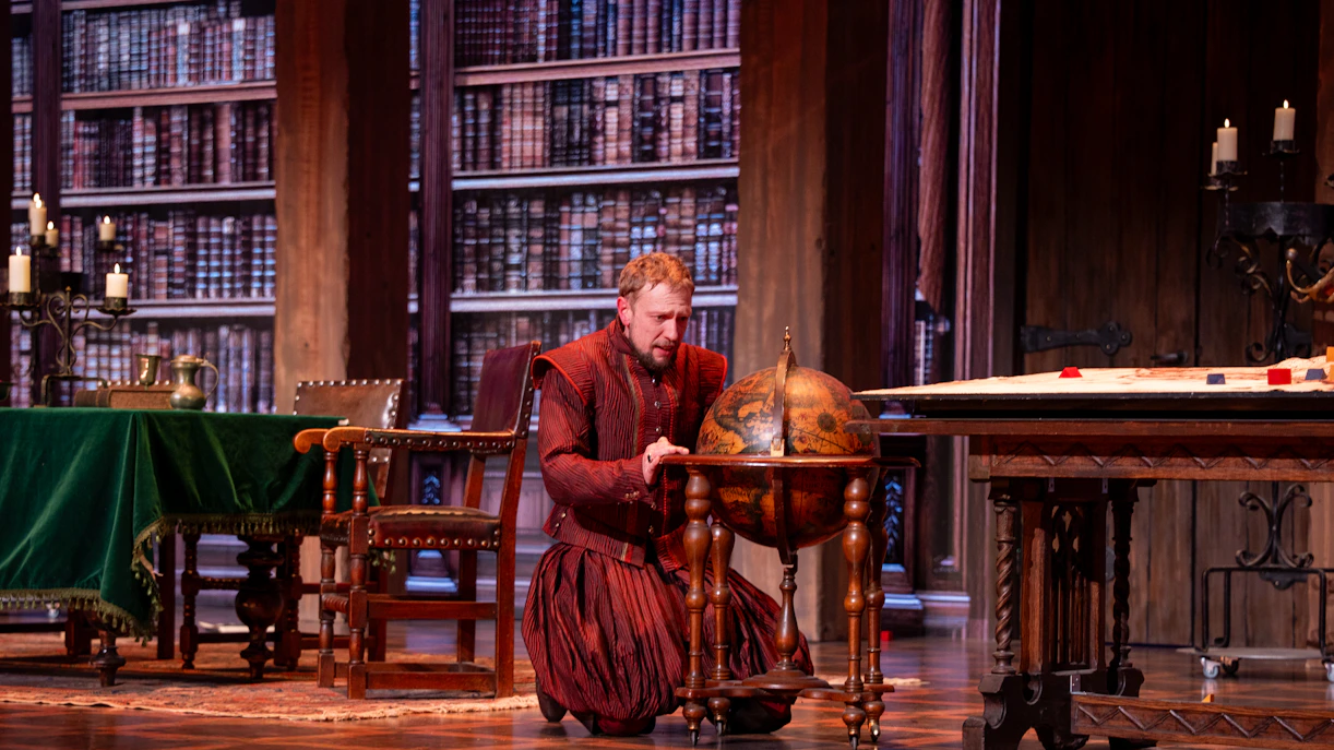 Man in historical attire examining a globe in a library setting, related to Willem van Oranje.