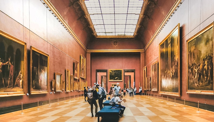 Tour group exploring the Denon Wing of the Louvre Museum in Paris, featuring iconic artworks and sculptures