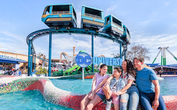 Family enjoying the DC Universe area at Six Flags Fiesta Texas with monorail above.