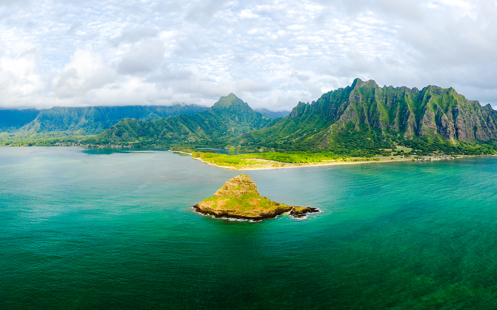 Aerial view of Kualoa Ranch, Hawaii with lush mountains and ocean.
