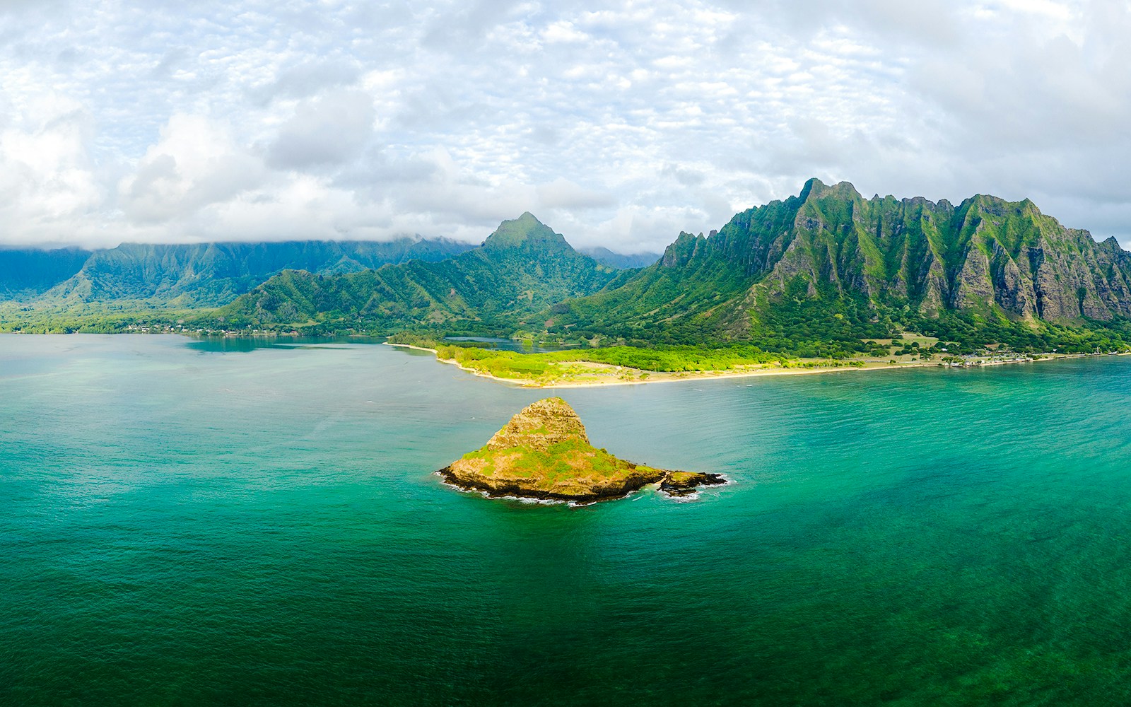 Aerial view of Kualoa Ranch, Hawaii with lush mountains and ocean.