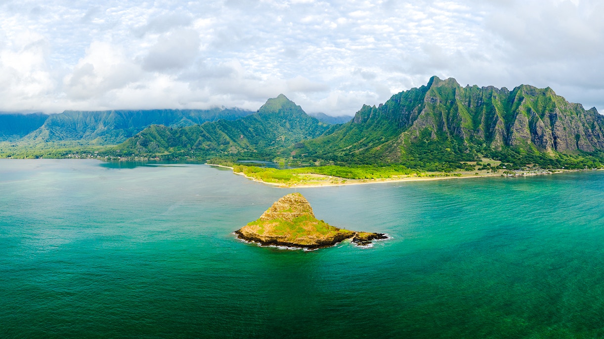 Aerial view of Kualoa Ranch, Hawaii with lush mountains and ocean.
