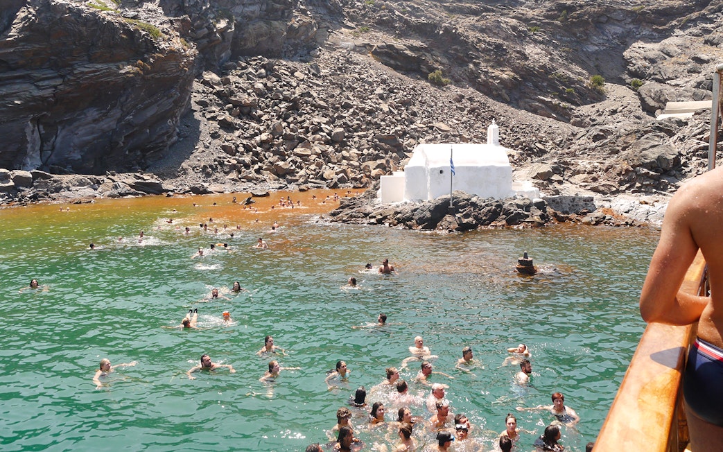 Guests swimming in hot springs near a white chapel during Santorini volcanic cruise tour.