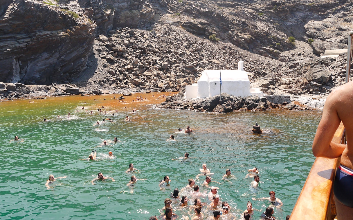 Guests swimming in hot springs near a white chapel during Santorini volcanic cruise tour.