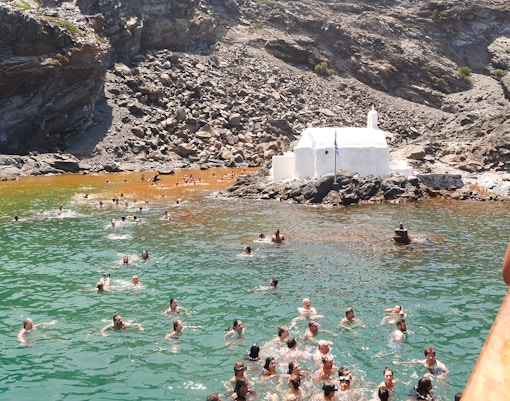 Guests swimming in hot springs near a white chapel during Santorini volcanic cruise tour.