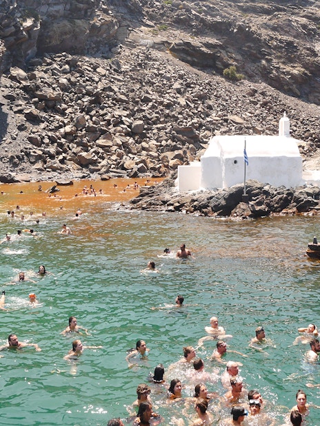 Guests swimming in hot springs near a white chapel during Santorini volcanic cruise tour.