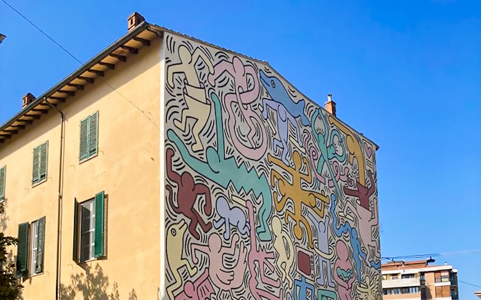 Colorful mural on a building in Pisa, Italy, featuring abstract figures and shapes.