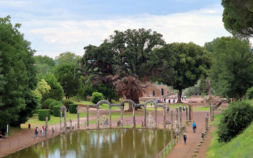 Reflecting pool and ancient ruins at Tivoli Villae, Italy, with visitors walking nearby.