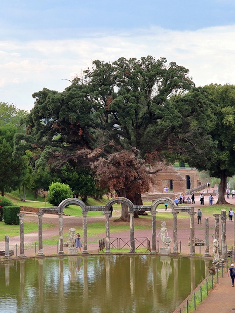 Reflecting pool and ancient ruins at Tivoli Villae, Italy, with visitors walking nearby.
