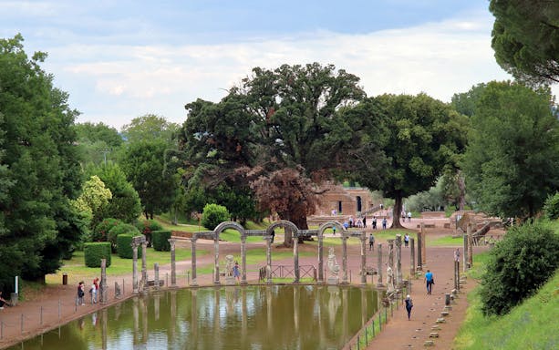 Reflecting pool and ancient ruins at Tivoli Villae, Italy, with visitors walking nearby.
