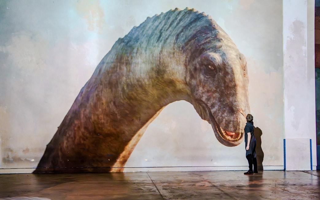 Person interacting with a dinosaur projection at Prehistoric Planet exhibition, Atelier des Lumières.