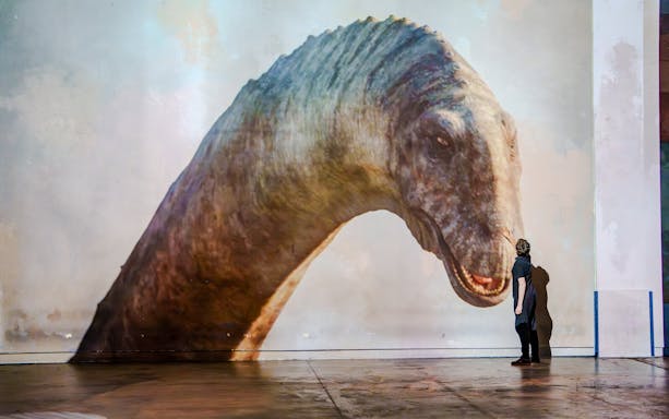 Person interacting with a dinosaur projection at Prehistoric Planet exhibition, Atelier des Lumières.